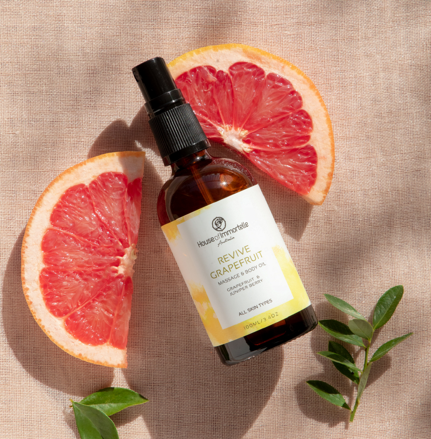 House of Immortelle Revive Grapefruit Massage Body Oil in a sleek bottle, infused with a refreshing grapefruit scent. The oil is designed to energize and revitalize the skin, with a smooth texture and invigorating fragrance, perfect for rejuvenating massages.