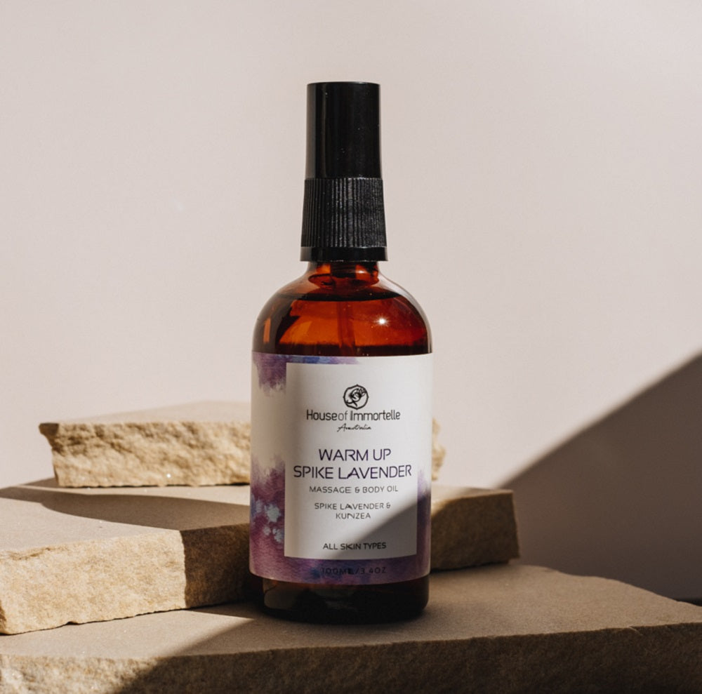 House of Immortelle Warm-Up Spike Lavender Massage Body Oil in a stylish bottle, infused with calming lavender and invigorating spices. The oil is designed to warm and relax muscles, with a smooth texture and a soothing fragrance, ideal for relieving tension and stress
